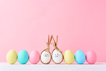 Colorful easter eggs with painted faces and bunny ears in row on a pink background