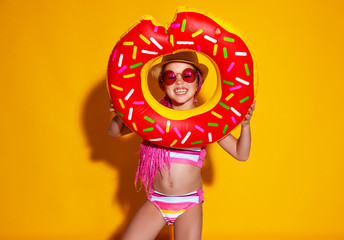 happy child girl in swimsuit with swimming ring donut on colored yellow background