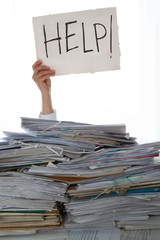 Person under a pile of papers with a hand holding a sign of help. Accounting.