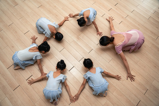 Ballet class. Chinese young children seating in the circle with teacher at the ballet school