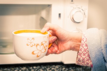 woman hand using are bringing coffe cup to the microwave oven at home. To reheat frozen food for their. Cooking made easy concept.