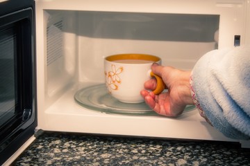 woman hand using are bringing coffe cup to the microwave oven at home. To reheat frozen food for their. Cooking made easy concept.