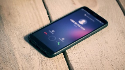 Woman take into hands ringing mobile phone lying on wooden board in close up
