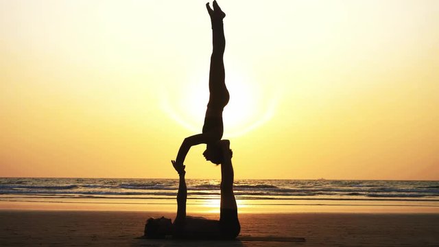 Silhouette of fit sporty couple practicing acrobatic yoga with partner together on the sandy beach. Female acrobat doing handstand on the hands of his lying male partner, close-up. 