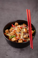 The concept of Japanese cuisine. Vegetarian noodles with tofu cheese and vegetables in a black ceramic plate. Red Chinese sticks. copy space