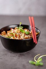The concept of Japanese cuisine. Vegetarian noodles with tofu cheese and vegetables in a black ceramic plate. Red Chinese sticks. copy space