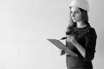 Black and white photo of a woman architect at the construction site with drawings and notebook
