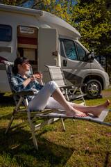 Woman is standing with a mug of coffee near the camper RV.