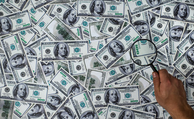 man holding magnifying Glass on the one hundred American Dollars background 
