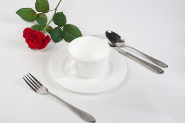 Festive table setting. White plate, fork, spoon and red rose.