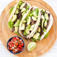 Corn tortillas with grilled beef, avocado, lime and salsa on wooden board. From above, top view, overhead.