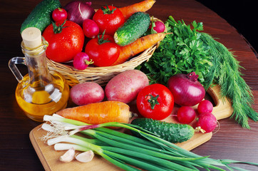 Appetizing vegetables and sunflower oil on a wooden table. Green onions, tomatoes, cucumbers, carrots, radishes, garlic, parsley.