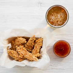 Chicken fingers with sour-sweet sauce and cold beer on a white wooden table, top view. Overhead, from above, flat lay.