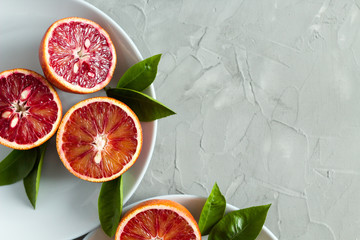 halves of fresh blood oranges with green leaves on a plate on a gray background. copy space. top...