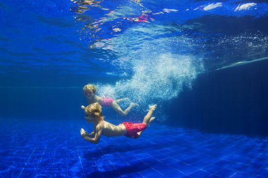 Happy family - funny kids learn to swim, dive underwater with fun. Jump with water splashes in pool. Healthy lifestyle, active people, sports activities, swimming classes on summer holidays with child