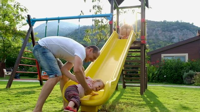 Funny Cute Baby Girl With Her Parents Playing On Playground Slide.