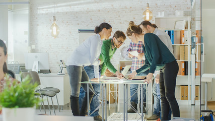 Group of Young Creative People Have Strategic Planning Session. They are Standing Near Big Glass Table with Open Laptops and Documents on the Table in their Bright and Modern Loft Office.