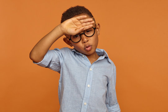 Human facial expressions and body language. Handsome African American male child in round eyeglasses having relieved look, breathing air out, making Phew sound, whiping sweat from his forehead