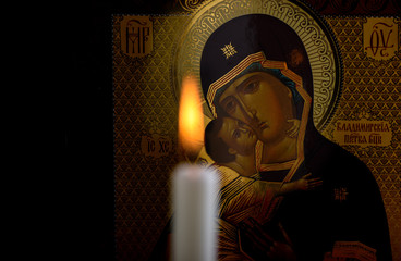 Orthodox icon of the Mother of God and baby Jesus and a blurred burning candle in front of icon