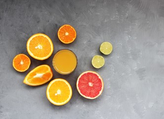 Bright citrus and a glass of juice on a grey textured background.
