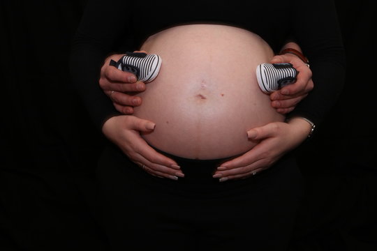 Babybauch (schwanger) mit Händen und Babyschuhen