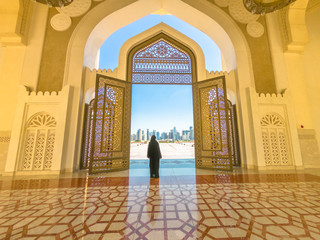 Woman with abaya dress looks at views of skyscrapers of Doha West Bay skyline outdoors State Grand...