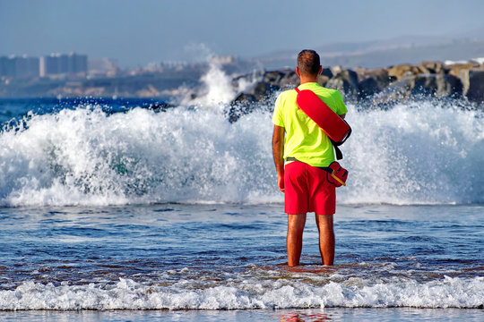 Undefined man in beach lifeguard uniform stands in the water and oversees order and the safety 