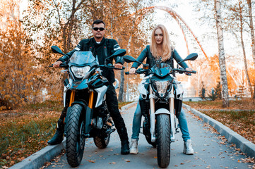 Fototapeta na wymiar An attractive guy and a young woman in a black leather outfit with a motorcycle.