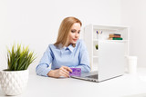 Office woman holding purple credit card and making shopping online at her workplace