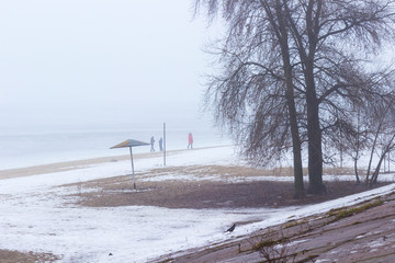 People on an empty spring beach by the river, trees and shelter from the sun. Foggy