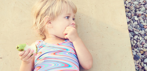 Cute adorable toddler girl eating fresh pear lying on the beach.