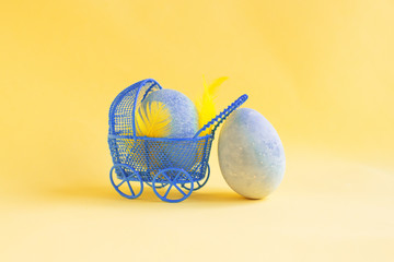 Blue Easter egg in a blue baby carriage. Near the second egg, like mom. Yellow background