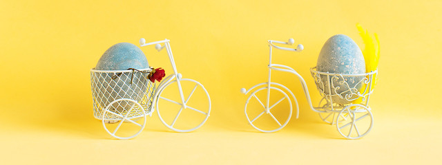 Two Easter eggs ride towards each other on bicycles on a yellow background.