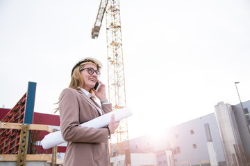 Frau als Architektin mit Helm, Bauplan, Plänen auf einer Baustelle mit Kran