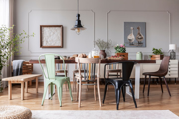 Colorful chairs at wooden table in grey rustic dining room interior with posters, flowers and table...