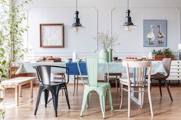 Colorful chairs at wooden table covered with light blue tablecloth in grey rustic dining room...