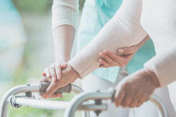 Closeup of grandmother's hands holding a walker and helpful granddaughter helping her