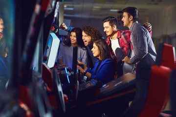 A group of friends playing arcade machine. - obrazy, fototapety, plakaty