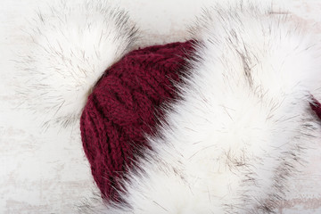 Red knitted winter hat with fur on white wooden background