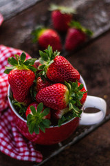 Seasonal fruit / harvest concept. View of a big red juicy strawberries in red cup on wooden table of organic berry farm. Summer fruit. Bay of Plenty, New Zealand 