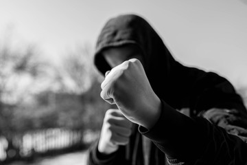 Unidentifiable teenage boy attacking with hes bare hands, focus on the fist in black and white,...