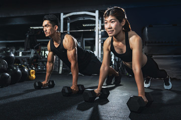 Fototapeta na wymiar Young couple is working out at gym. Attractive woman and handsome muscular man are training in light modern gym. Doing plank on kettlebell. Push-up on weights