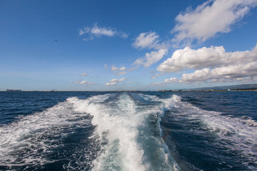 Wake water of a fast ferry speedboat with white foam, blue sky and deep blue sea on a sunny summer day