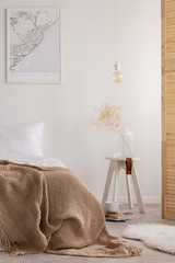 Vertical view of map on the wall of stylish bedroom with bedding made from natural materials and wooden bedside table, real photo