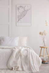 White sheets and blanket on comfortable bed in simple bedroom with wooden bedside table and map on the wall