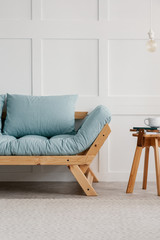 Stylish wooden sofa with light blue pillows next to small wooden coffee table with magazines and coffee cup, real photo