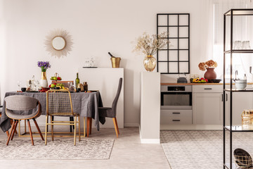 Stylish open plan kitchen and dining room interior with white cupboard and long table with grey tablecloth and food