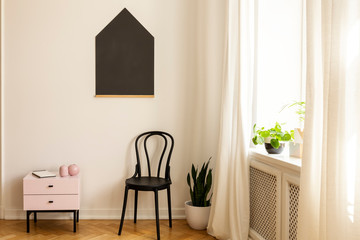 Black poster above cabinet and chair in white simple teenager's room interior with plants. Real photo