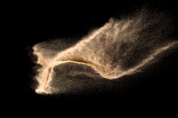 Dry river sand explosion. Brown color sand splash against black background. Yellow sand fly wave in the air.