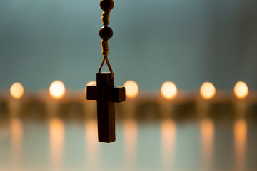 The cross of a christian/ catholic rosary in the foreground with a background of burning candles....